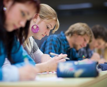 pretty female college student sitting in a classroom full of students during class (shallow DOF; color toned image)